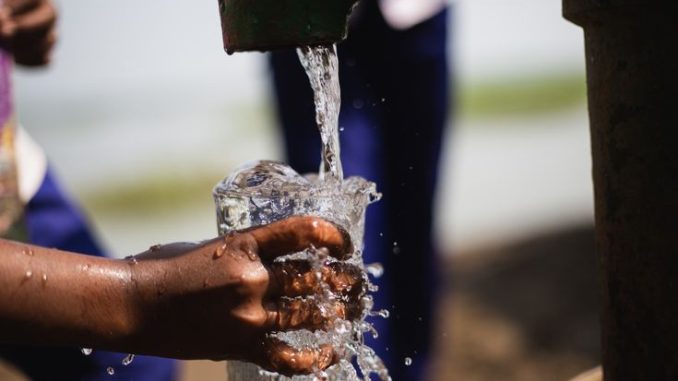 Closeup of a child hand collecting fresh drinking water from local tube-well. A hand of a kid collecting drinking water with a glass. Splash and sprinkle of water falling on glass.
